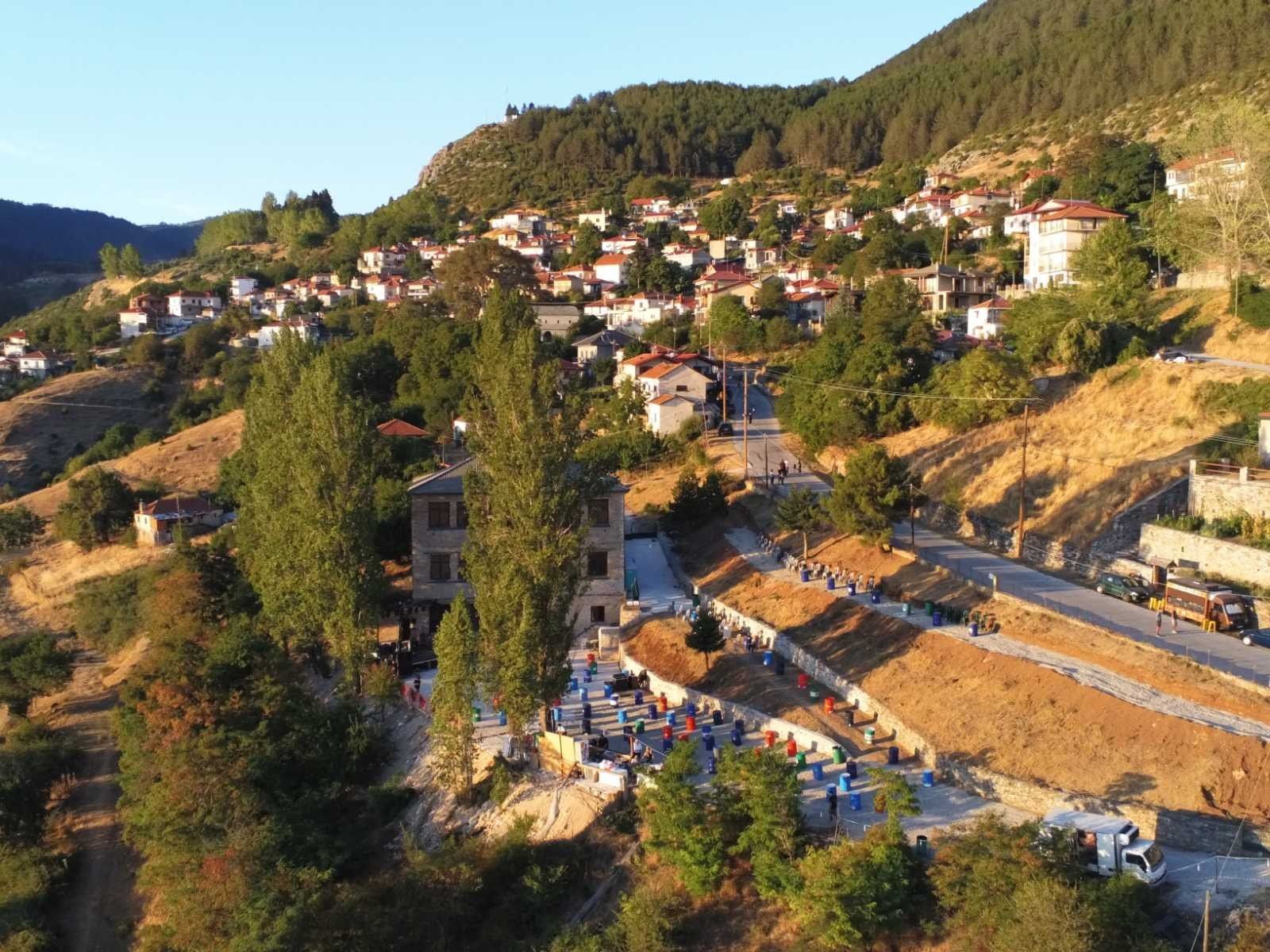 Αεροφωτογραφία του Κοκκινοπηλού στην πλαγιά του βουνού στο ηλιοβασίλεμα, με καρέκλες στημένες για υπαίθρια συναυλία.